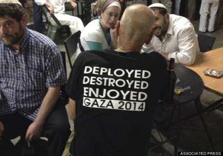 An Israeli army reservist officer, back on camera, wearing a T-shirt referring to the Israeli forces' operations during the war in Gaza, talks with others outside a bar in Jerusalem, early Wednesday, Aug. 13, 2014. Egypt presented a proposed cease-fire to Israel and Hamas aimed at ending the monthlong war, Palestinian officials said early Wednesday after negotiators huddled for a second day of Egyptian-mediated talks meant to resolve the crisis and bring relief to the embattled Gaza Strip. (AP Photo/Lefteris Pitarakis)